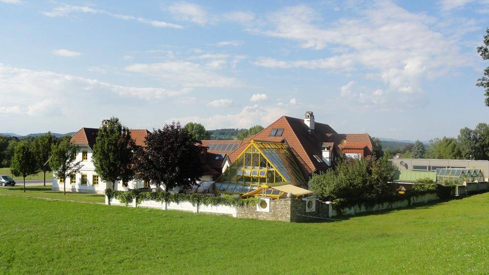 Weitläufiges Anwesen mit großem Wintergarten, umgeben von grünen Feldern unter blauem Himmel.