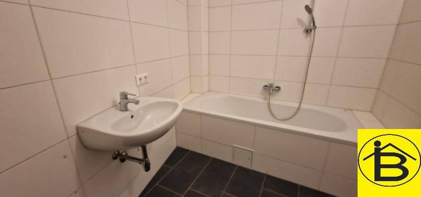 Funktionales Badezimmer mit Badewanne und Waschbecken, hell gefliest und pflegeleicht.