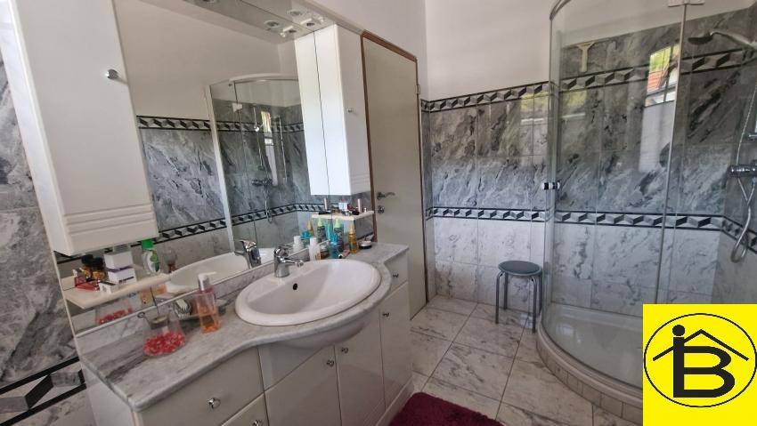 Badezimmer mit Duschkabine, Einzelwaschbecken und Marmorfliesen.