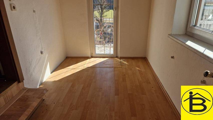 Heller Raum mit Holzboden und Zugang zu einem Außenbereich durch eine Glastür, sonnig.