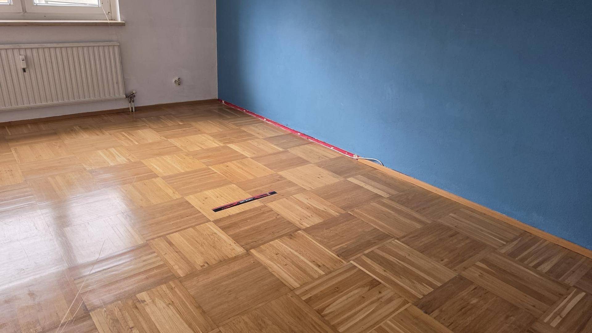 Geräumiger Raum mit Parkettboden und einer auffälligen blauen Akzentwand.