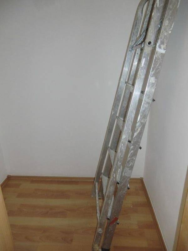Leerer Raum mit hellem Laminatboden und einer Leiter, möglicherweise im Umbau oder als Abstellraum genutzt.