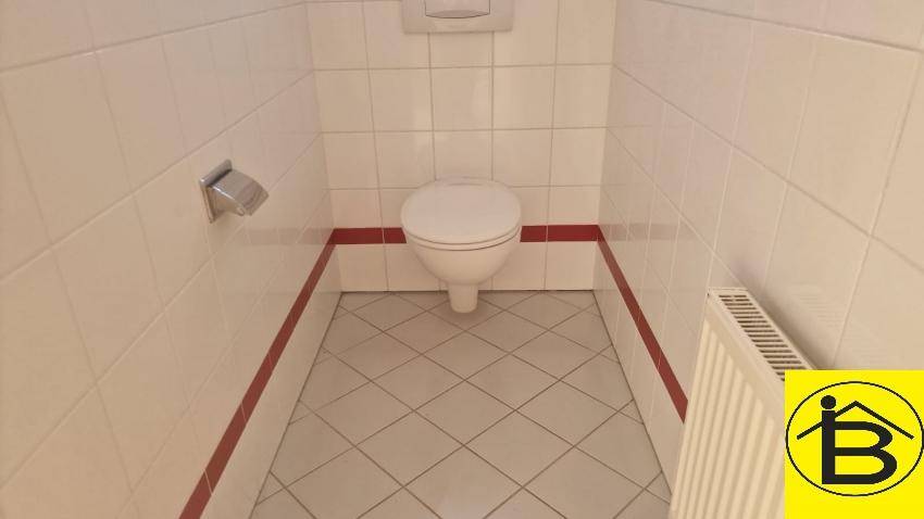 Kleines WC mit Wand-WC, Fliesenboden und Heizkörper, in sauberem Zustand.