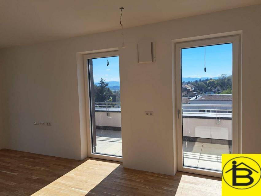 Lichtdurchfluteter Raum mit Holzboden und Zugang zu einem Balkon, mit weitem Ausblick auf die Umgebung.