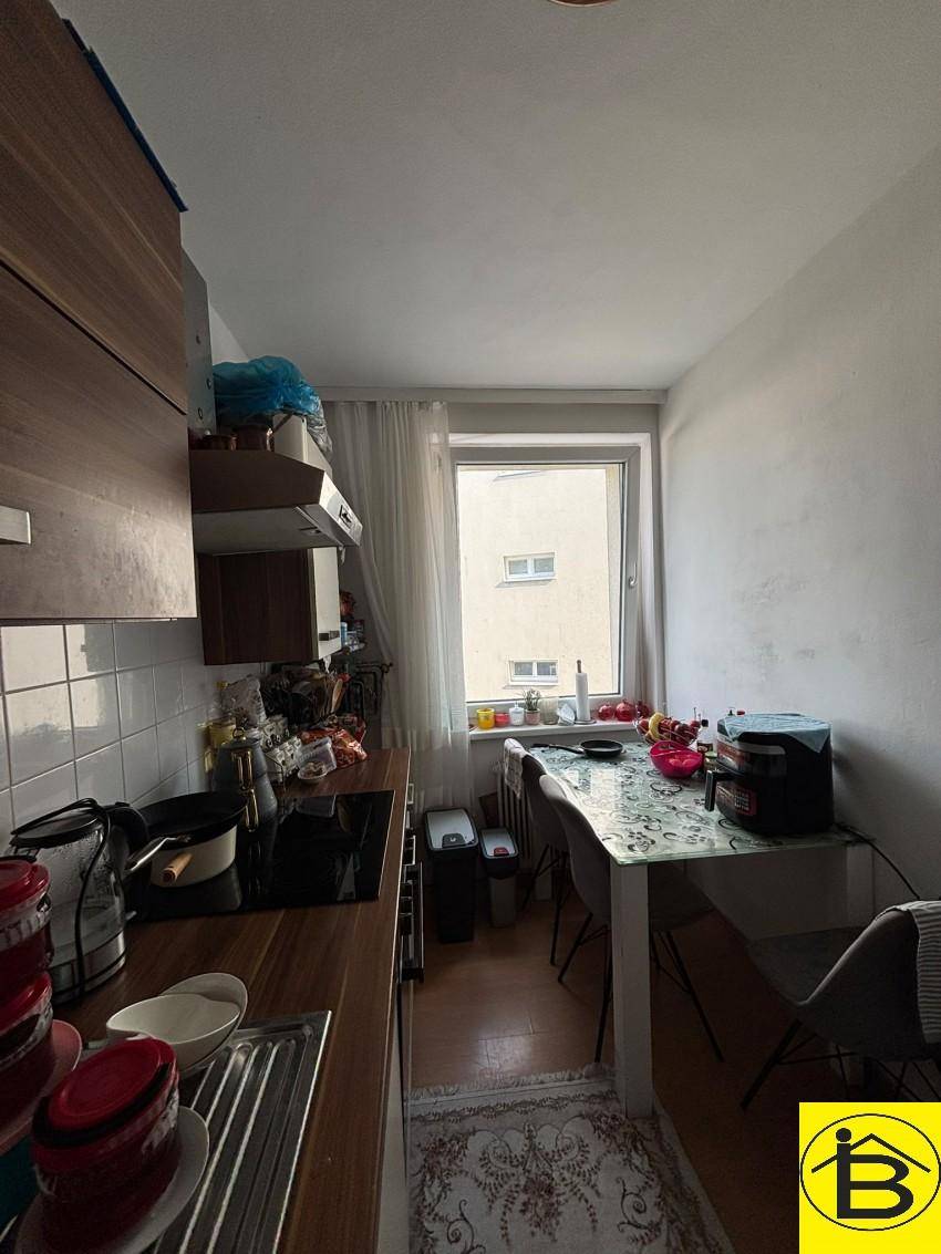 Helle Küche mit Essbereich am Fenster, ausgestattet mit modernen Geräten und Holztheke.