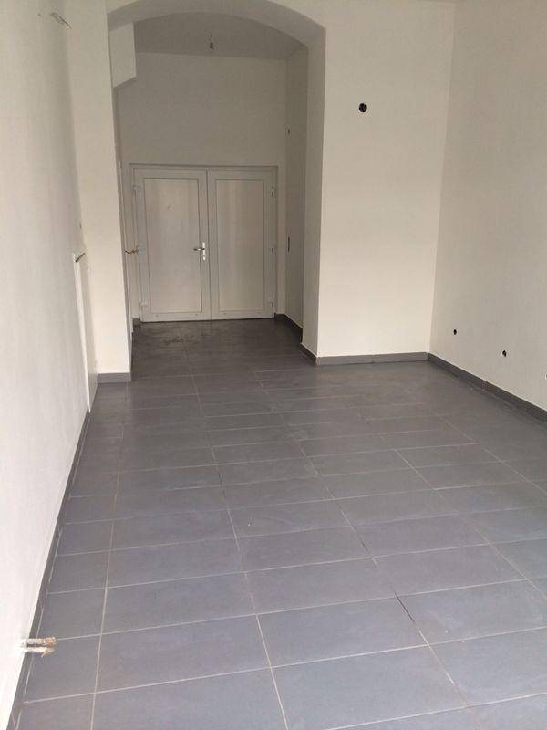 Leerer Raum mit Fliesenboden und weiß gestrichenen Wänden, führt zu weiteren Bereichen.
