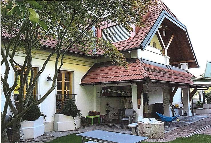 Überdachter Außenbereich mit kleinem Garten, Tischtennisplatte und schattenspendenden Bäumen.