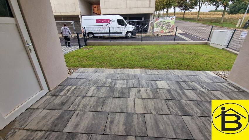 Private Terrasse mit modernen Pflastersteinen und angrenzender kleiner Rasenfläche im Freien.