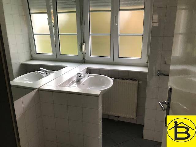 Badezimmer mit zwei Waschbecken, einem großen Spiegel, Fliesenboden und einem Fenster mit Rollläden.