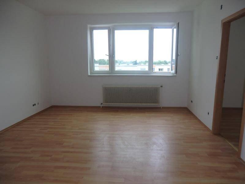 Geräumiges Zimmer mit Laminatboden, großen Fenstern und Blick auf die städtische Umgebung.