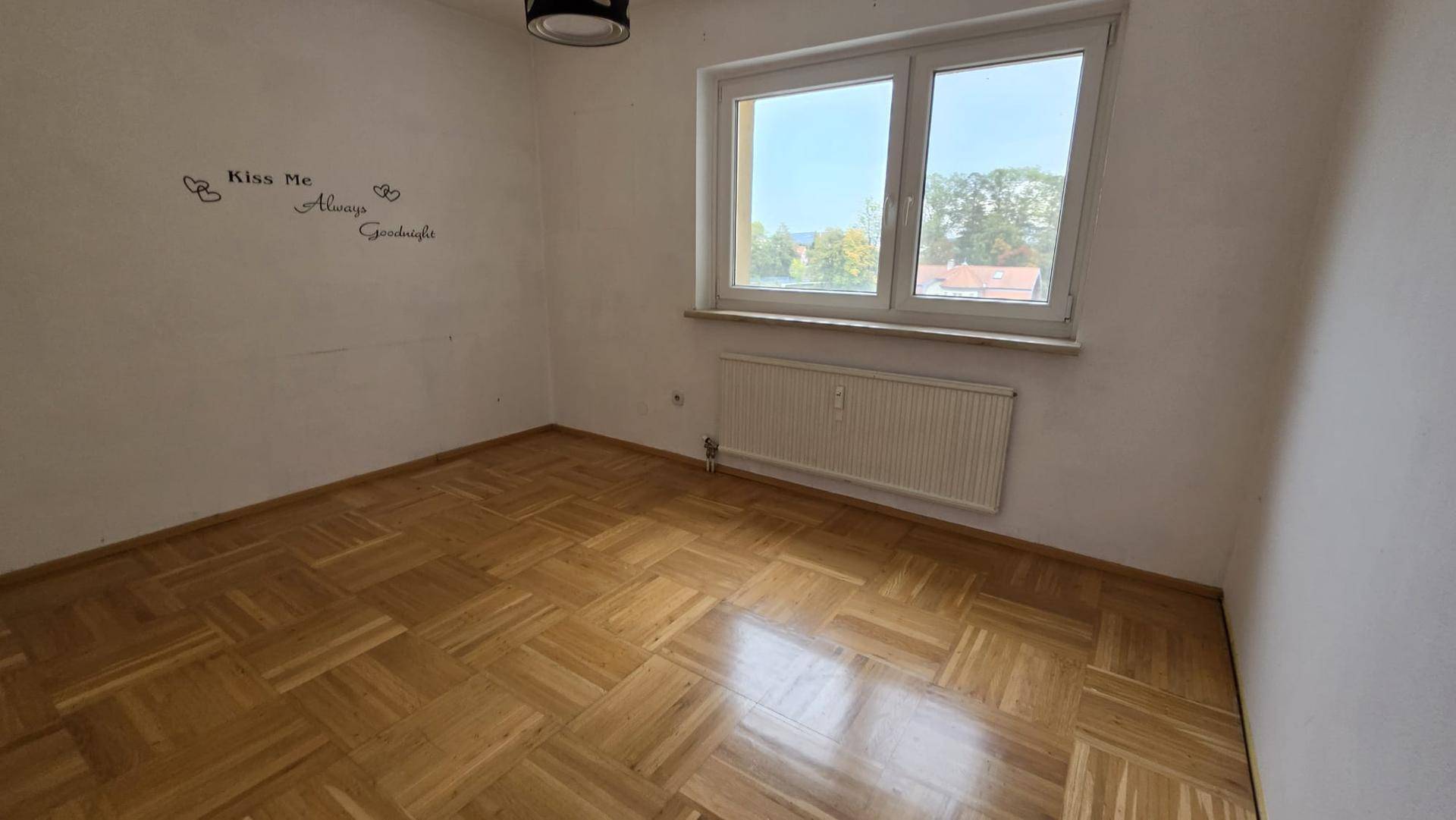 Gemütliches Schlafzimmer mit hellem Parkettboden und einem großen Fenster für viel Tageslicht.