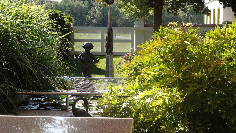 Nahaufnahme eines Gartenteichs mit Statue und üppiger Bepflanzung in der Grünanlage.