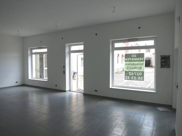 Heller Innenraum mit großen Fenstern und grauen Fliesen, bereit für individuelle Gestaltung.