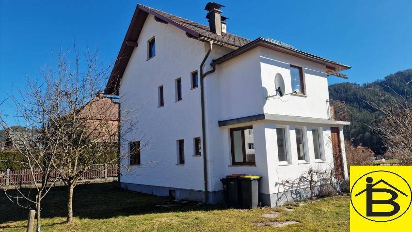 Rückansicht des Hauses mit Satteldach, Balkon und Blick auf die umliegende Landschaft und Berge.