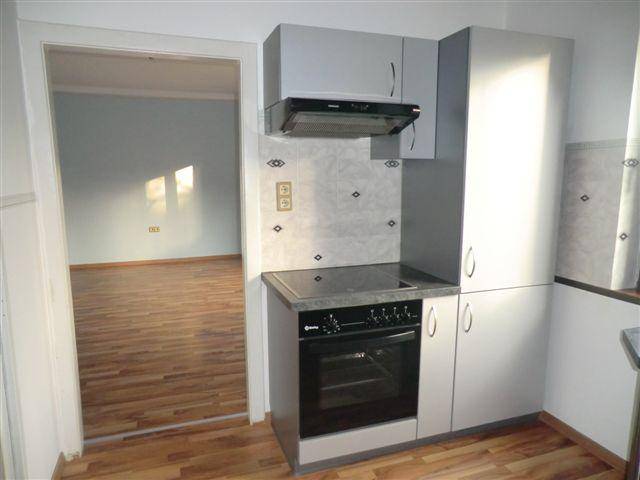 Küchenzeile mit Herd, Backofen und Dunstabzugshaube, angrenzend an ein helles Zimmer.