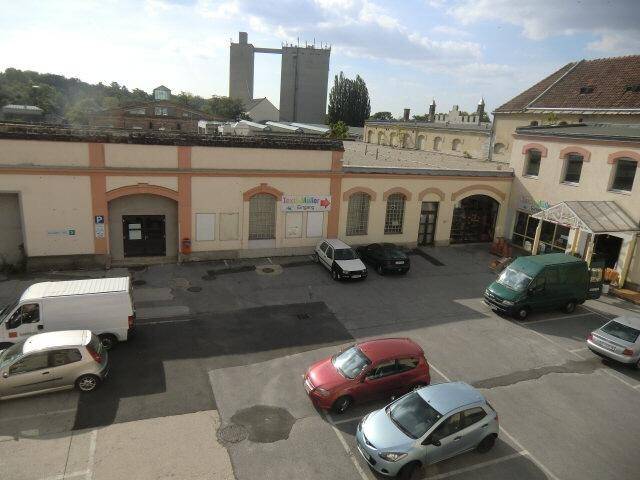 Innenhof mit geparkten Autos und umliegenden Gebäuden, im Hintergrund eine Industrieanlage.