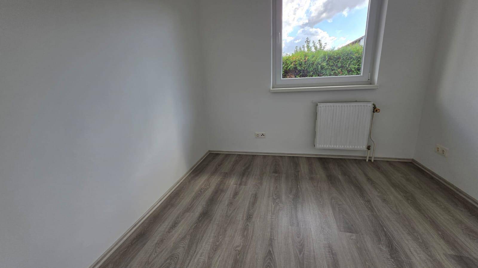 Geräumiges Schlafzimmer mit Laminatboden und Fenster, das viel Tageslicht hereinlässt.