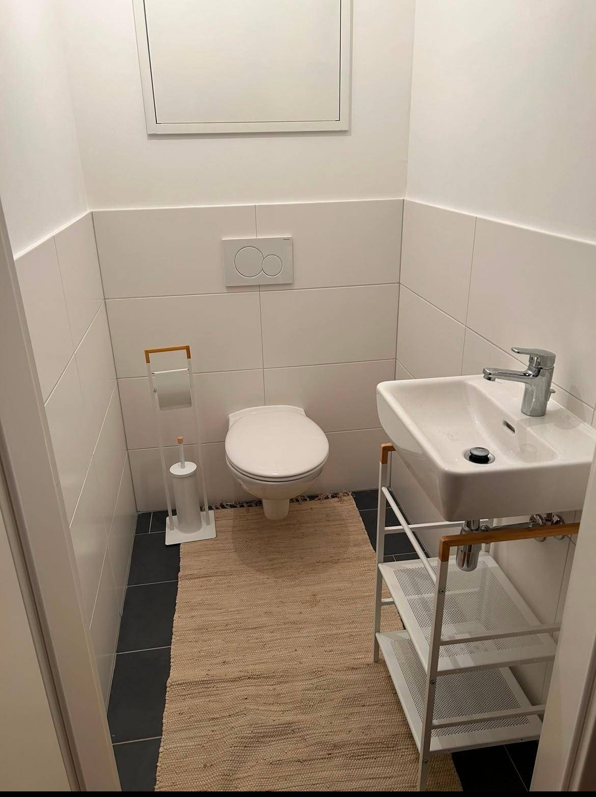 Modernes Gäste-WC mit wandhängender Toilette, kleinem Waschbecken und Fliesenboden.
