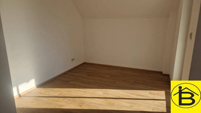 Leeres Zimmer mit Holzboden und weiß gestrichenen Wänden, das viel natürliches Licht erhält.