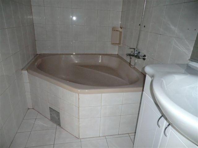 Badezimmer mit beigefarbener Eckbadewanne und weißen Fliesen an Wänden und Boden.