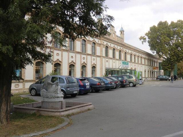 Historisches Gebäude mit vielen Fenstern und Parkplätzen davor, umgeben von Bäumen.