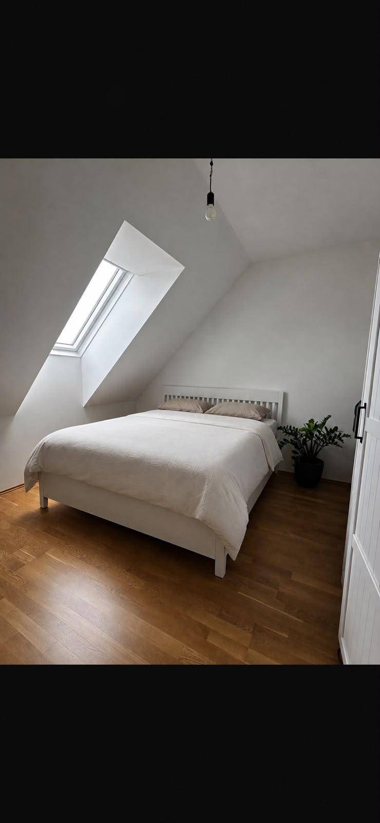Helles Schlafzimmer mit Bett, Holzfußboden und einem Dachfenster, das viel Licht hereinlässt.