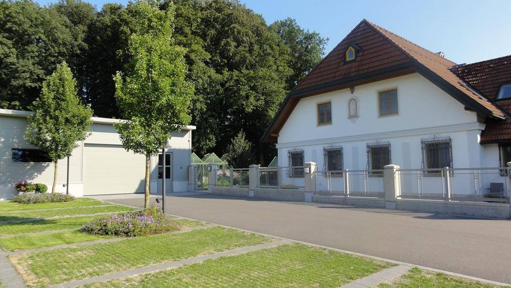 Gebäudefassade mit Garage, Zufahrt und jungen Bäumen in einer gepflegten Außenanlage.