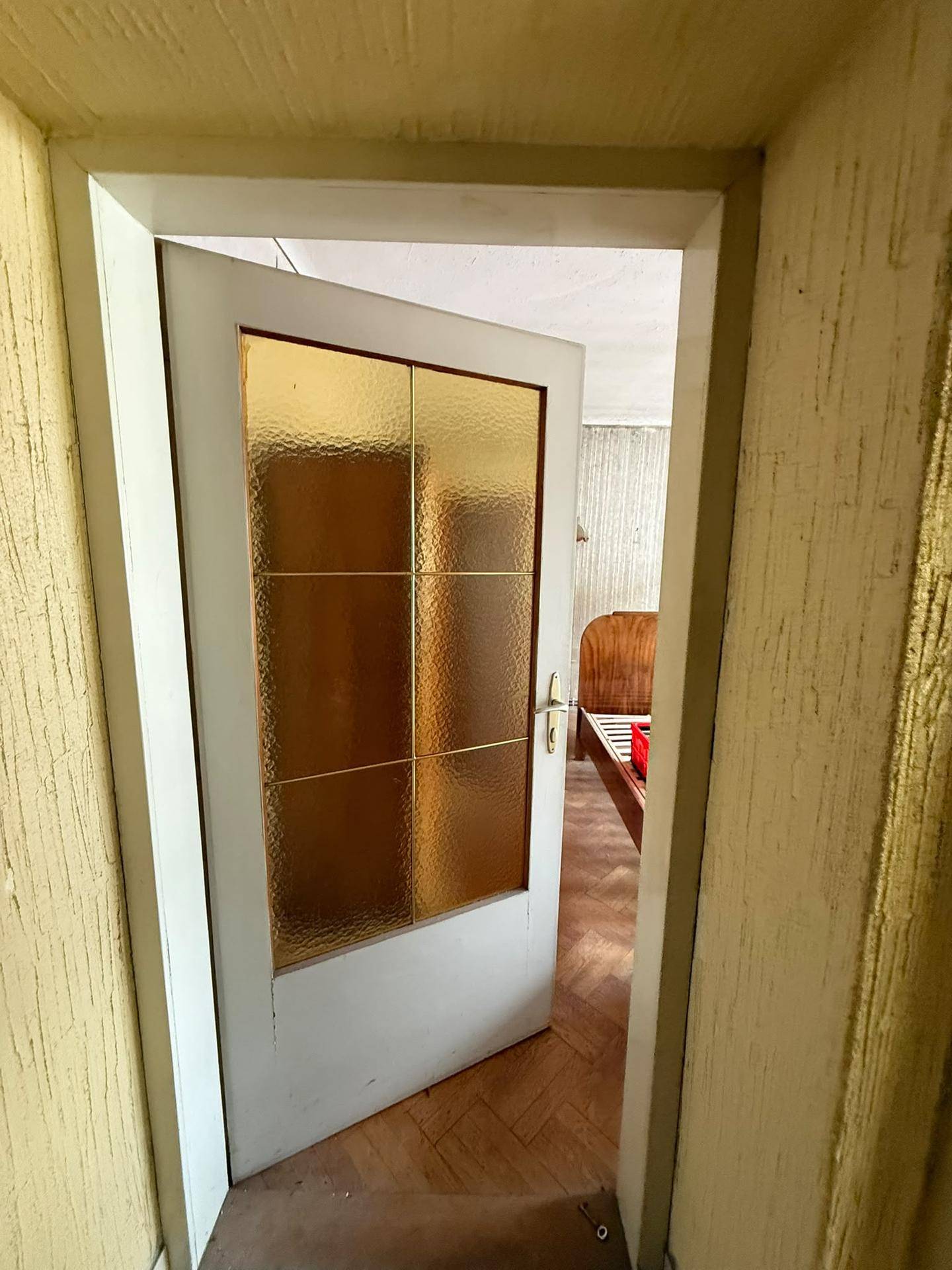 Blick durch eine offene Tür in ein Zimmer mit Parkettboden und einem Bettrahmen.