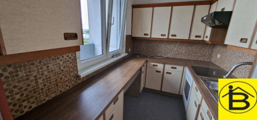Ältere Küche mit beigen Schränken, brauner Arbeitsplatte und Fensterblick.