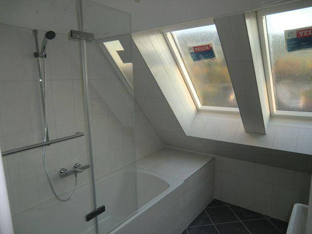 Modernes Badezimmer im Dachgeschoss mit Badewanne, Dusche und zwei Dachfenstern.
