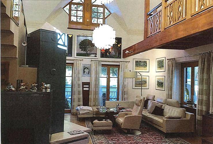 Großzügiges Wohnzimmer mit hohen Decken, Galerie, großen Fenstern und einem Kachelofen.