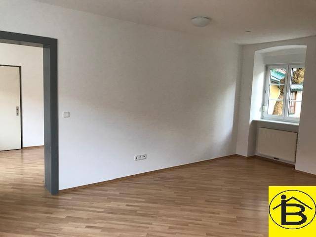 Heller, leerer Raum mit Holzparkettboden und einem Fenster, das viel Tageslicht hereinlässt.