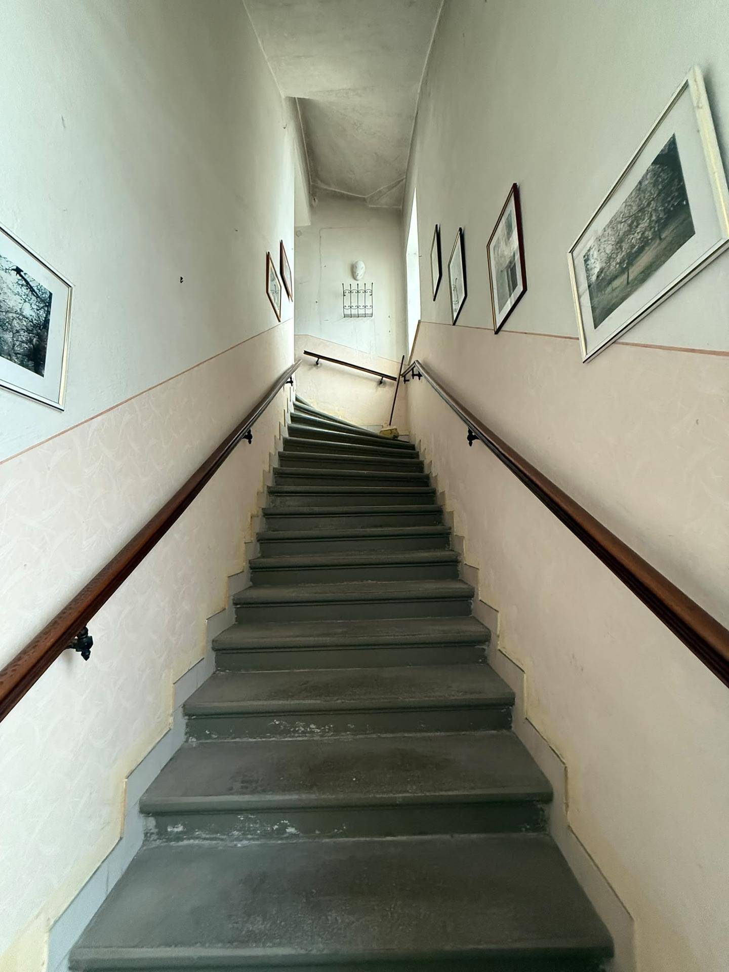 Treppenhaus mit Steinstufen, Holzgeländer und gerahmten Bildern an den Wänden.