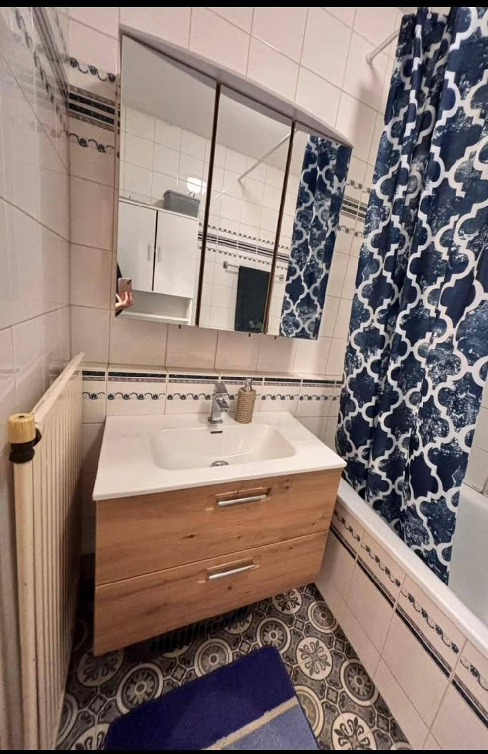 Badezimmer mit modernem Waschtischunterschrank, Spiegelschrank und Badewanne mit Duschvorhang in blauem Muster.