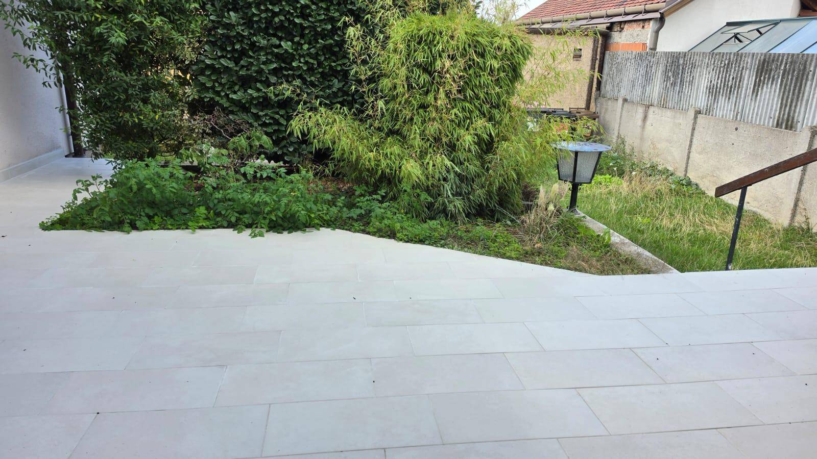 Gepflasterte Terrasse mit angrenzendem Grünbereich und einem Gartenweg.