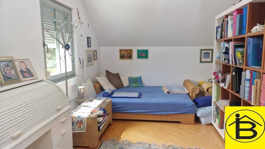 Helles Gästezimmer oder Büro mit Einzelbett, Bücherregal und Holzboden.