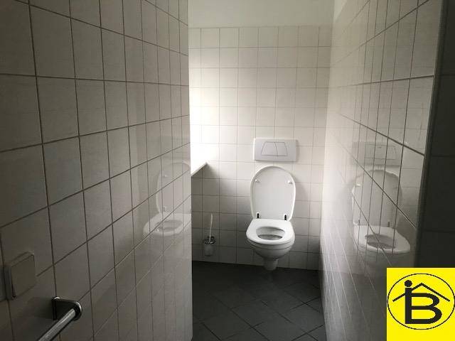 Separate Toilette mit wandmontiertem WC, weißen Fliesen an den Wänden und dunklem Fliesenboden.