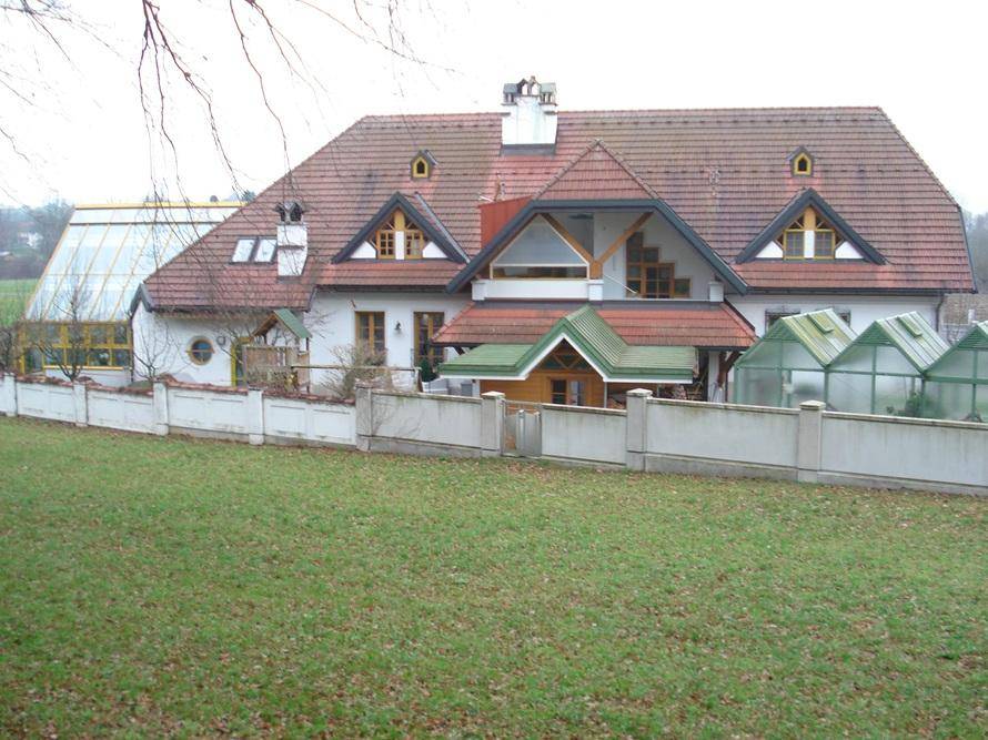 Anwesen aus der Ferne mit Wintergarten, Gewächshäusern und umgebender Grünfläche.