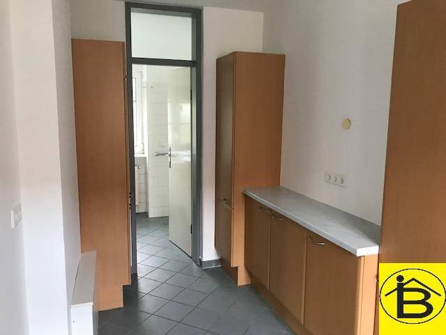 Funktionaler Raum mit braunen Schränken, einer Arbeitsplatte und Fliesenboden, der zu einem weiteren Raum führt.