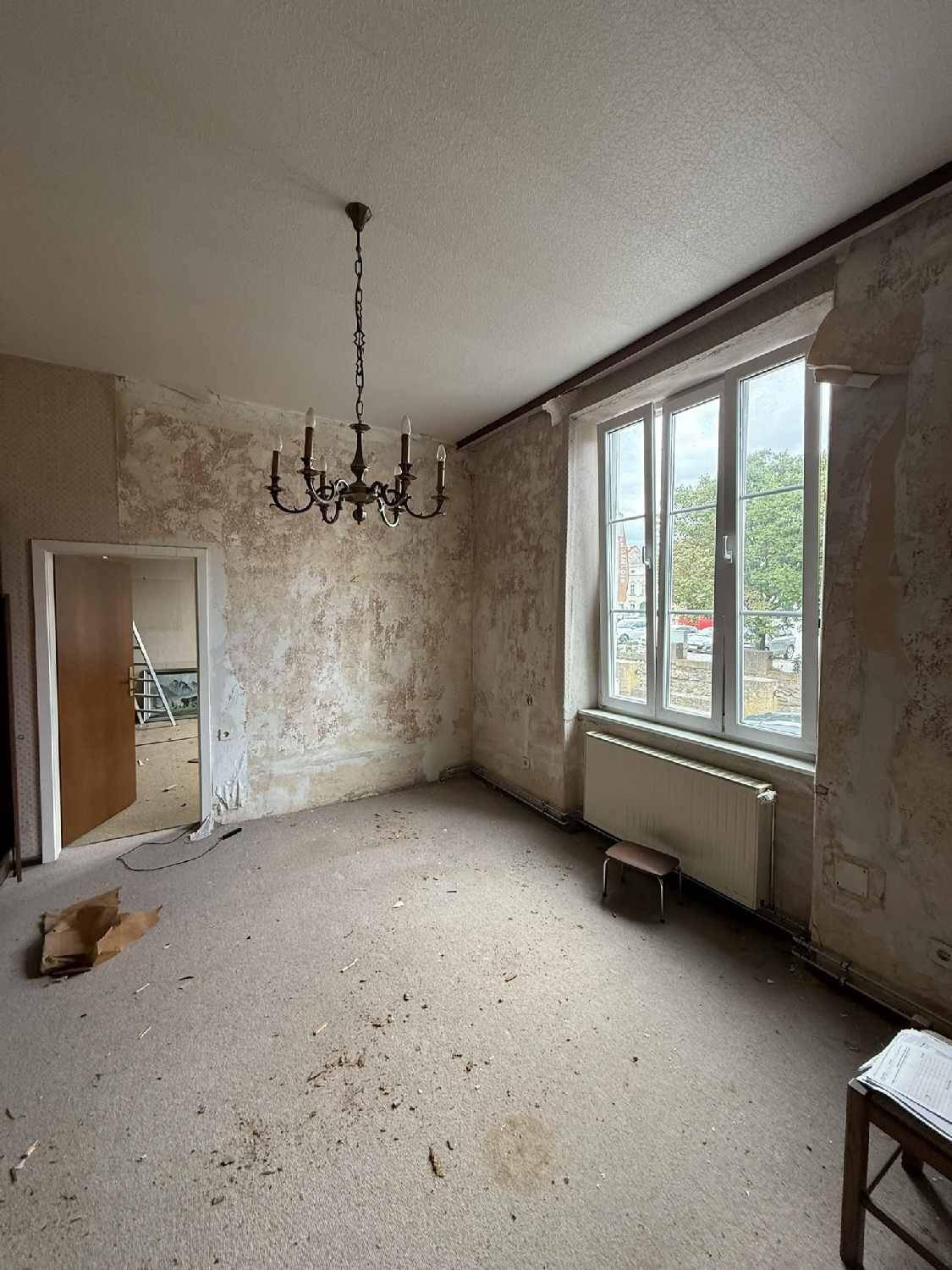 Leeres Zimmer mit einem Kronleuchter und einem großen Fenster, bereit zur Renovierung.