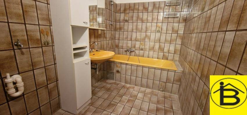 Badezimmer mit braunen Fliesen, gelber Badewanne und passendem Waschbecken.