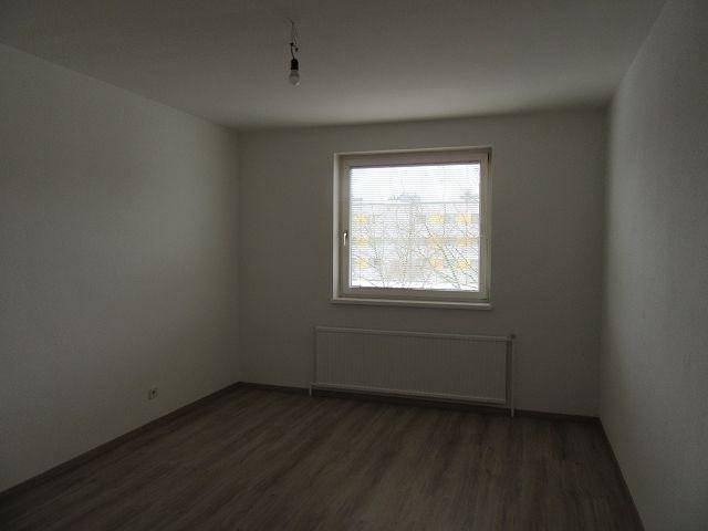 Helles Zimmer mit Fenster und dunklerem Laminatboden, vielseitig nutzbar für verschiedene Wohnbedürfnisse.