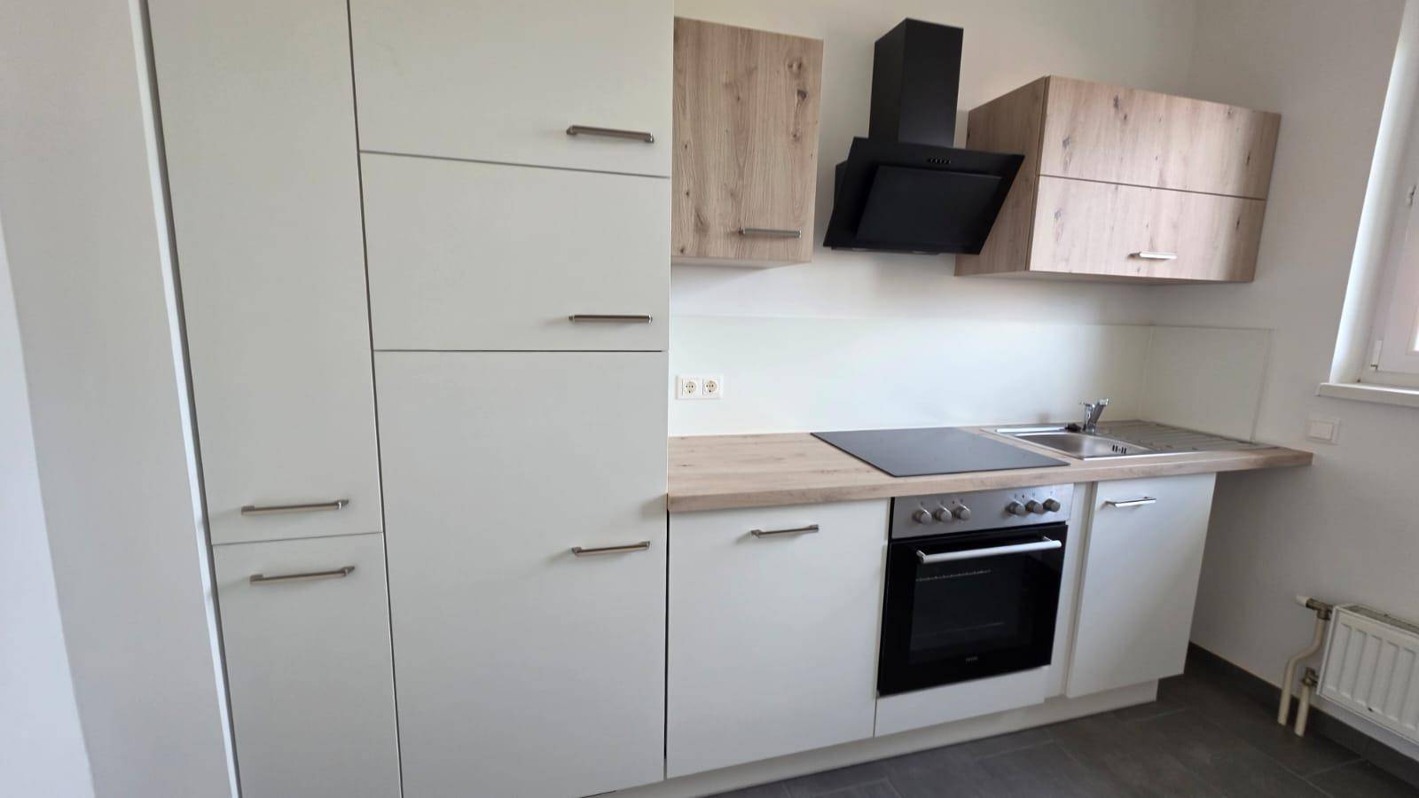 Moderne Einbauküche mit weißen Schränken, Holzarbeitsplatte, Induktionskochfeld und Dunstabzugshaube.