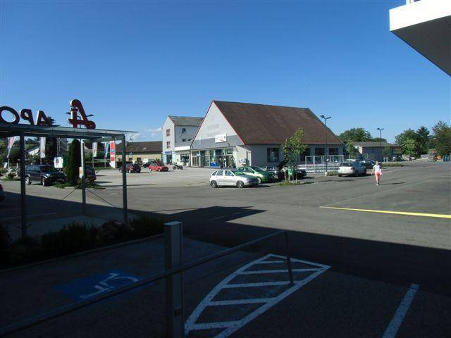 Weitläufiger Parkplatz vor Geschäftsgebäuden unter klarem blauem Himmel an einem sonnigen Tag.