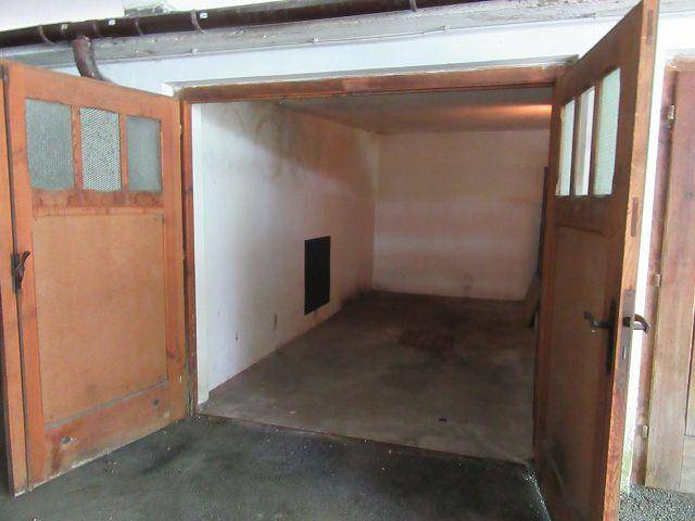 Geräumige Garage mit geöffneten Holztüren und sauberem Betonboden, ideal für Fahrzeuge.