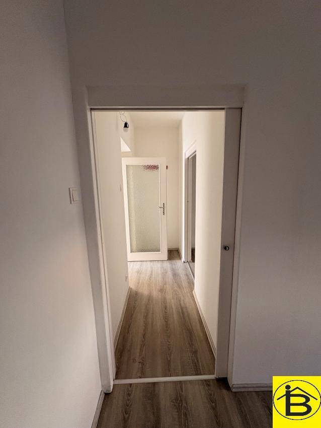 Langer Flur mit Laminatboden und weiß gestrichenen Wänden, der die verschiedenen Bereiche verbindet.