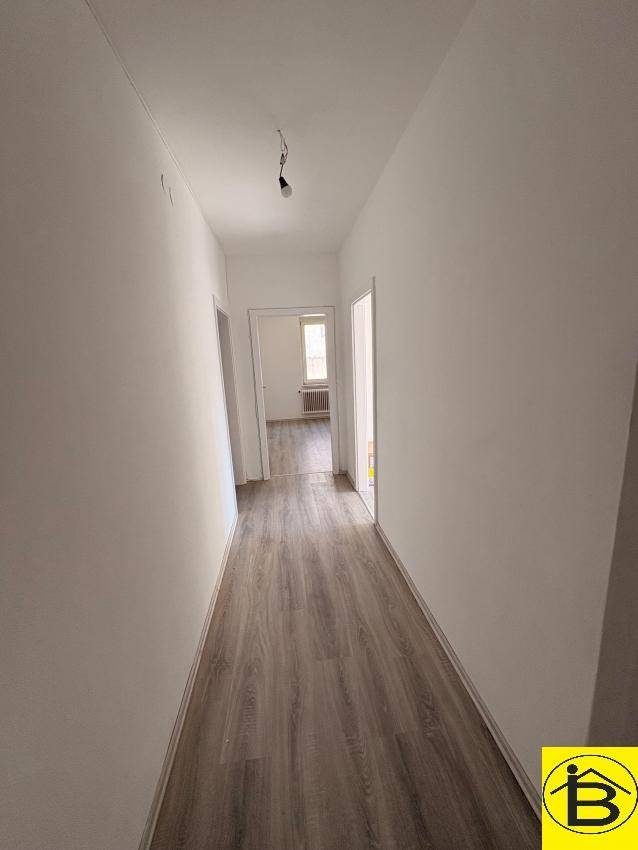 Langer, heller Flur mit Laminatboden, der zu den verschiedenen Zimmern der Wohnung führt.