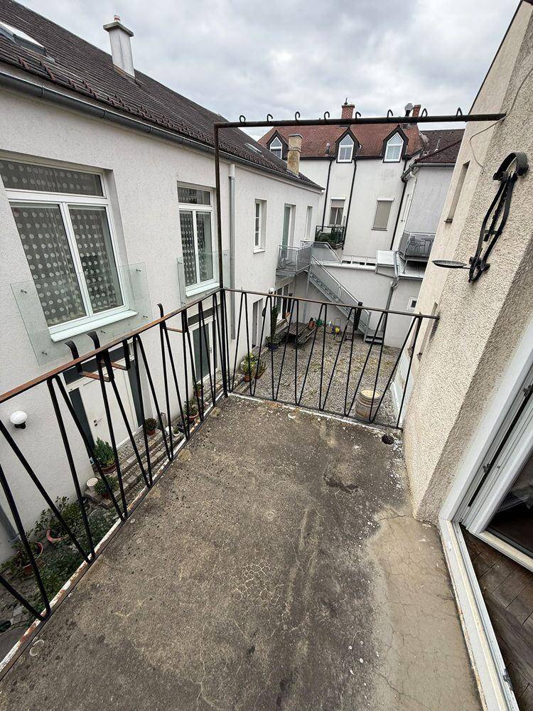Balkon mit Blick auf einen Innenhof, mit Betonboden und schmiedeeisernem Geländer.