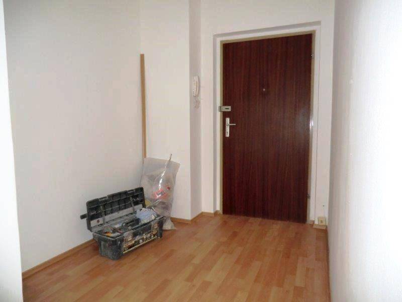 Eingangsbereich mit Laminatboden und einer stabilen Holztür, die zur Wohnung führt.