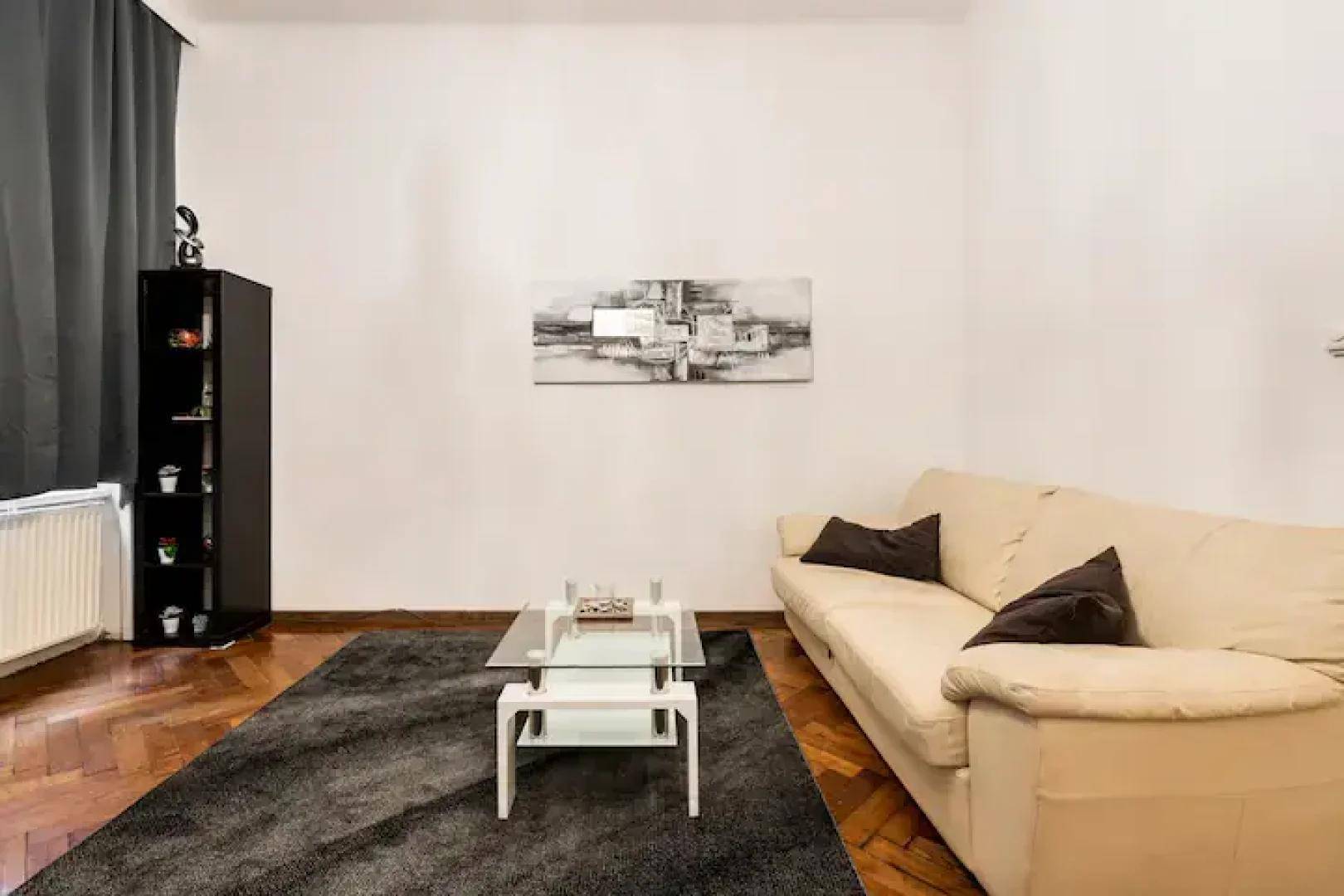 Gemütliches Wohnzimmer mit hellem Sofa, Couchtisch und Parkettboden, ergänzt durch einen Teppich.